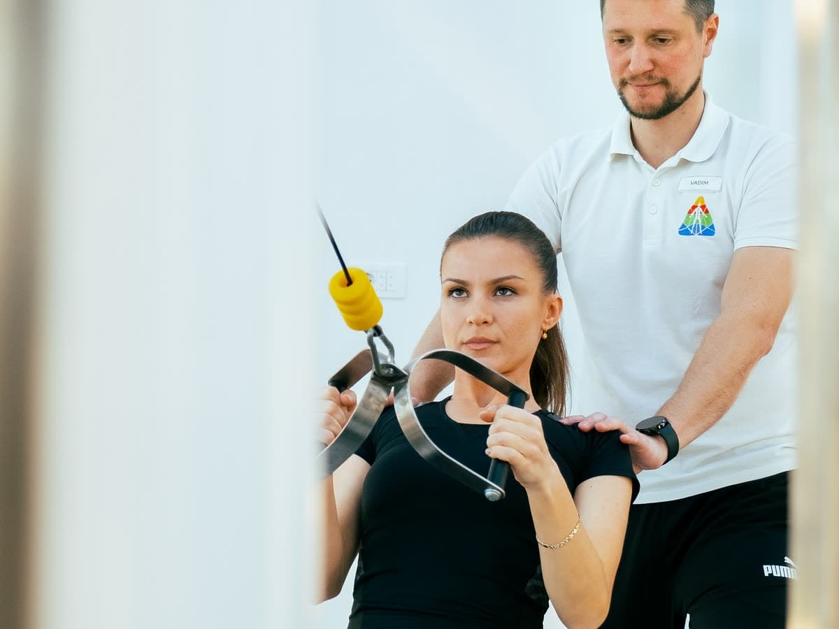 A seated patient working a cable machine while a therapist watches the movement